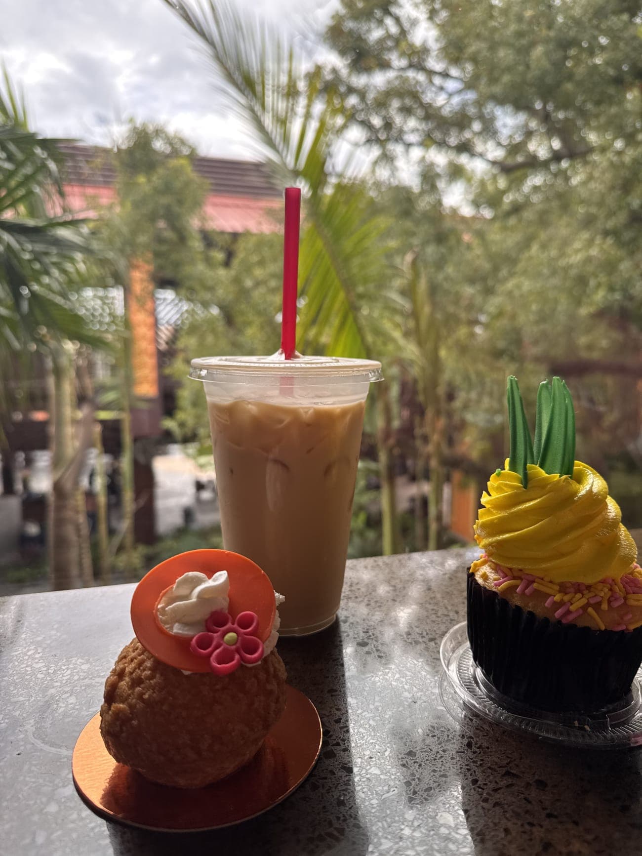 Full breakfast spread from Kona Island with choux, iced coffee, and Aloha cupcake against palm trees