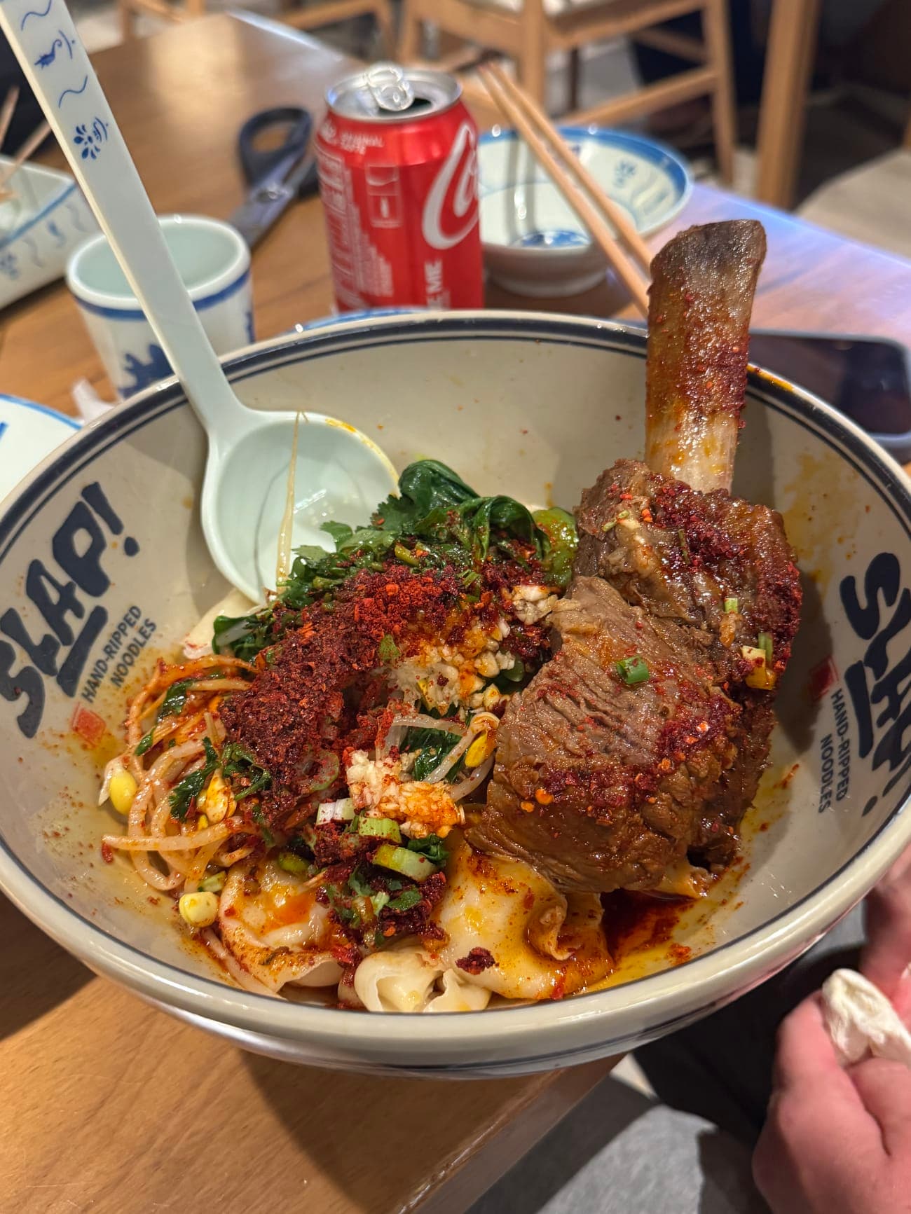 Beef short rib chili slap noodles with a massive bone-in fall-off-the-bone short rib towering over the bowl at SLAP Hand-Ripped Noodles