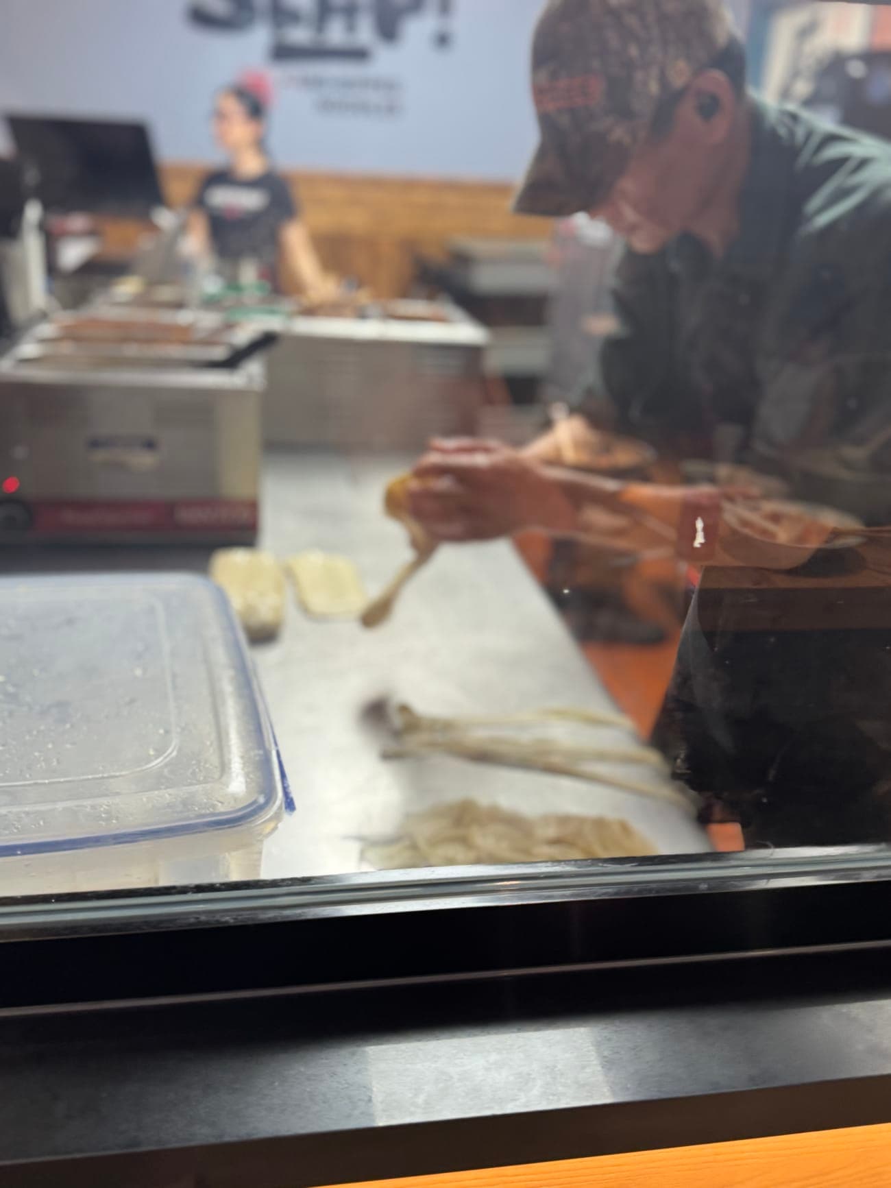 Chef pulling and stretching dough behind the open kitchen window at SLAP Hand-Ripped Noodles in Orlando
