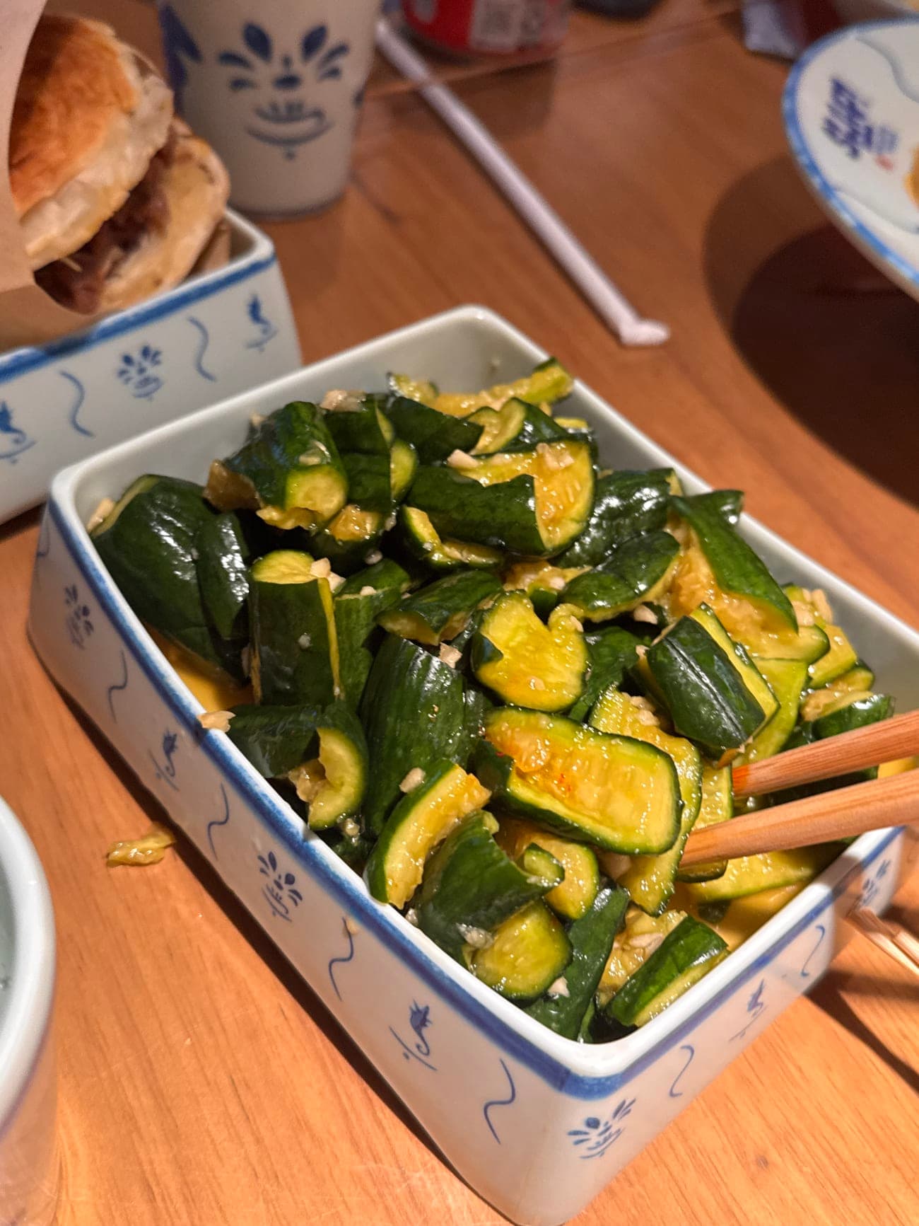 Smashed cucumber garlic salad with chopped garlic and chili oil in a blue and white ceramic dish at SLAP Hand-Ripped Noodles