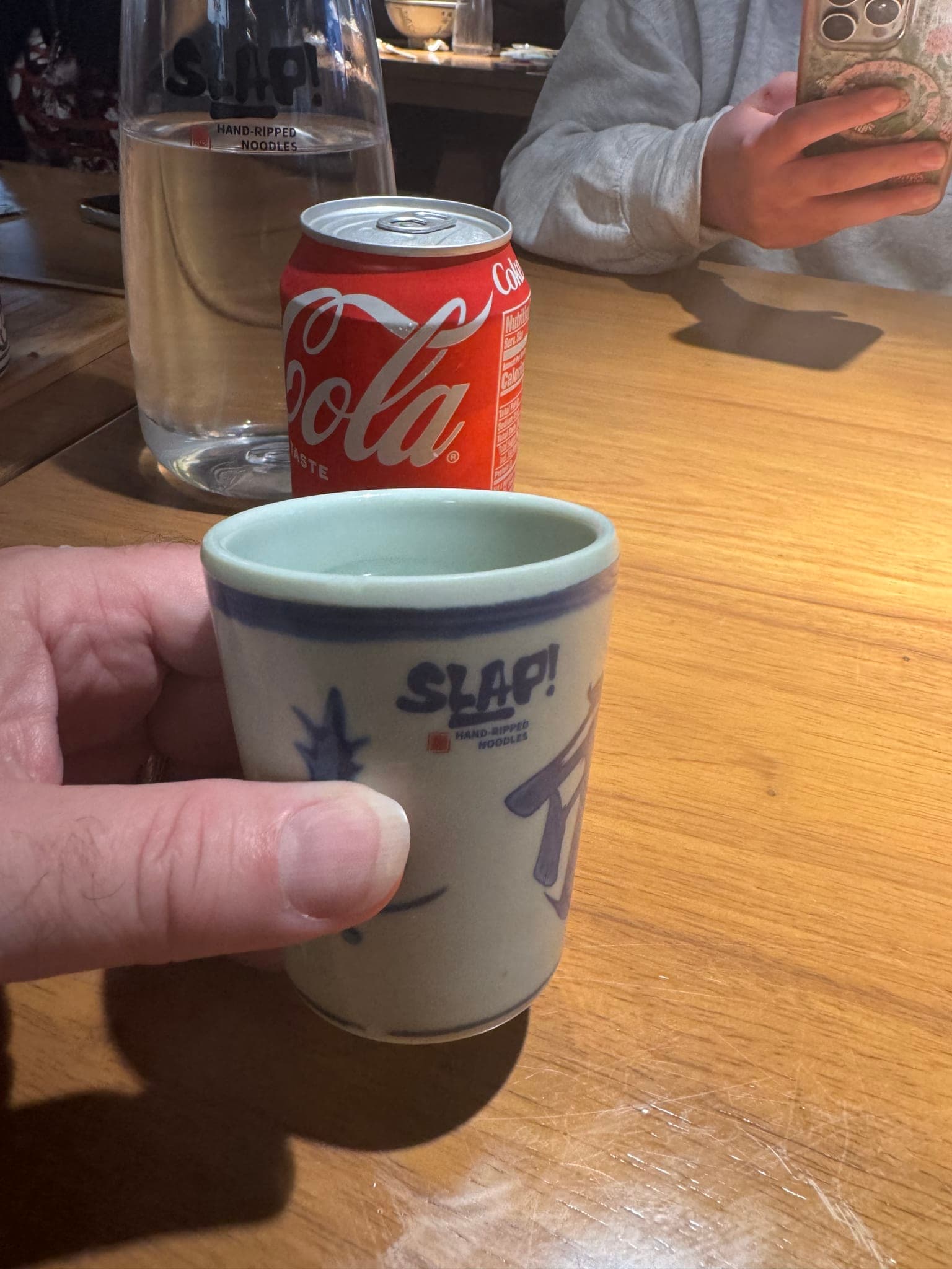 Hand holding a small blue and white SLAP-branded ceramic tea cup at the Orlando hand-ripped noodle shop