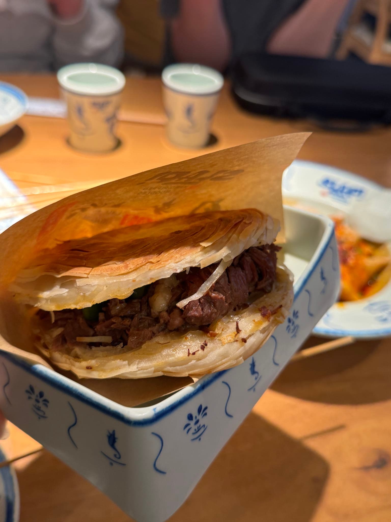Side view of a layered crispy pancake sandwich packed with braised beef at SLAP Hand-Ripped Noodles in Orlando