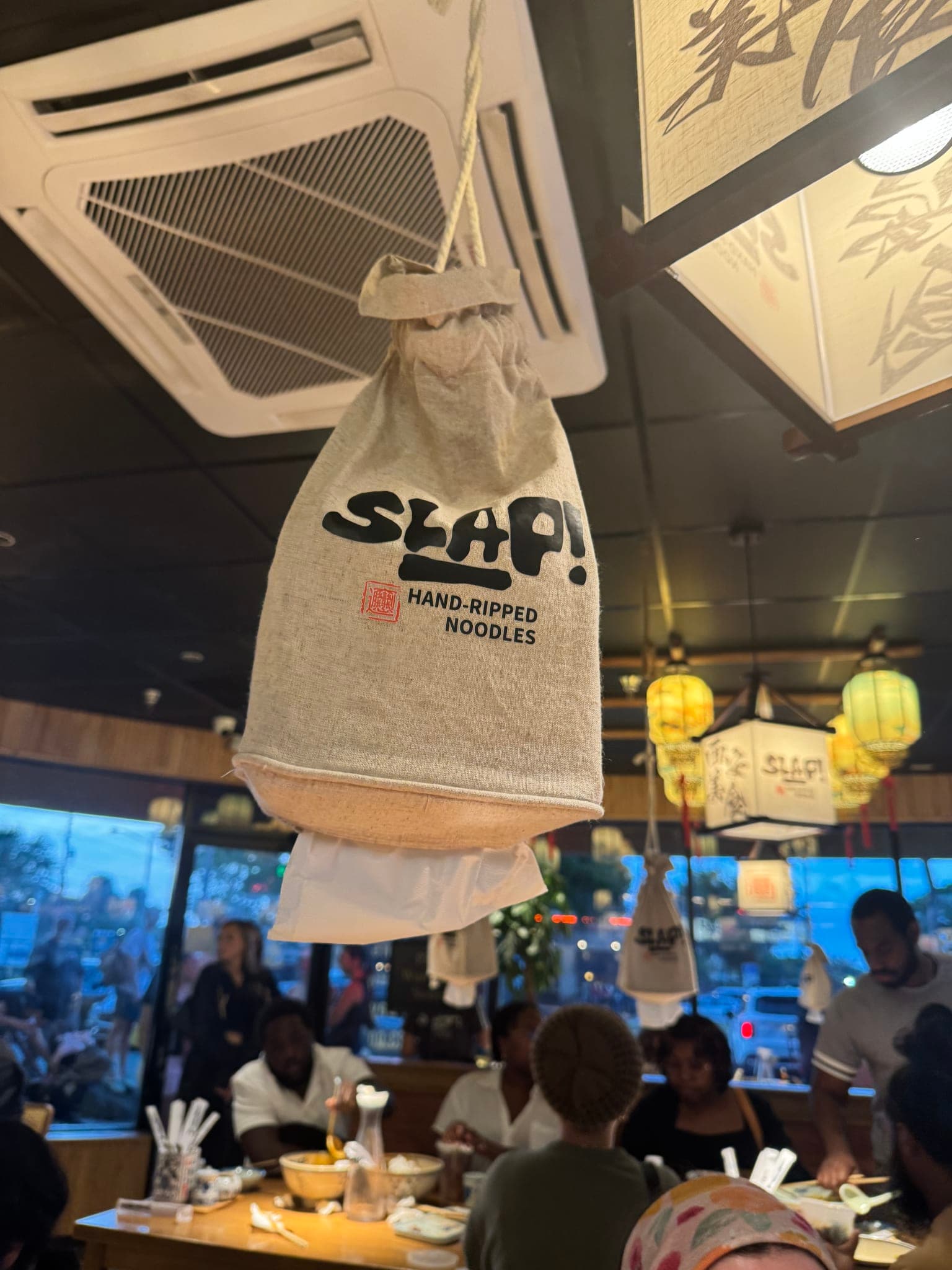 Linen SLAP Hand-Ripped Noodles napkin sack hanging above a packed dining room of guests at the Orlando restaurant