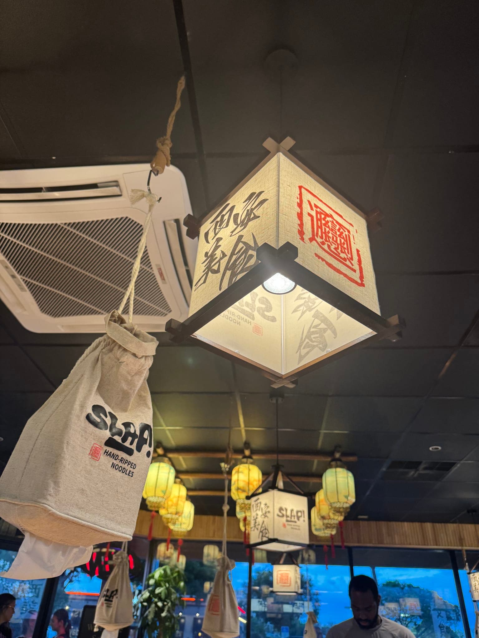 Hanging paper lantern with Chinese calligraphy and SLAP linen napkin sacks suspended from the ceiling at SLAP Hand-Ripped Noodles in Orlando