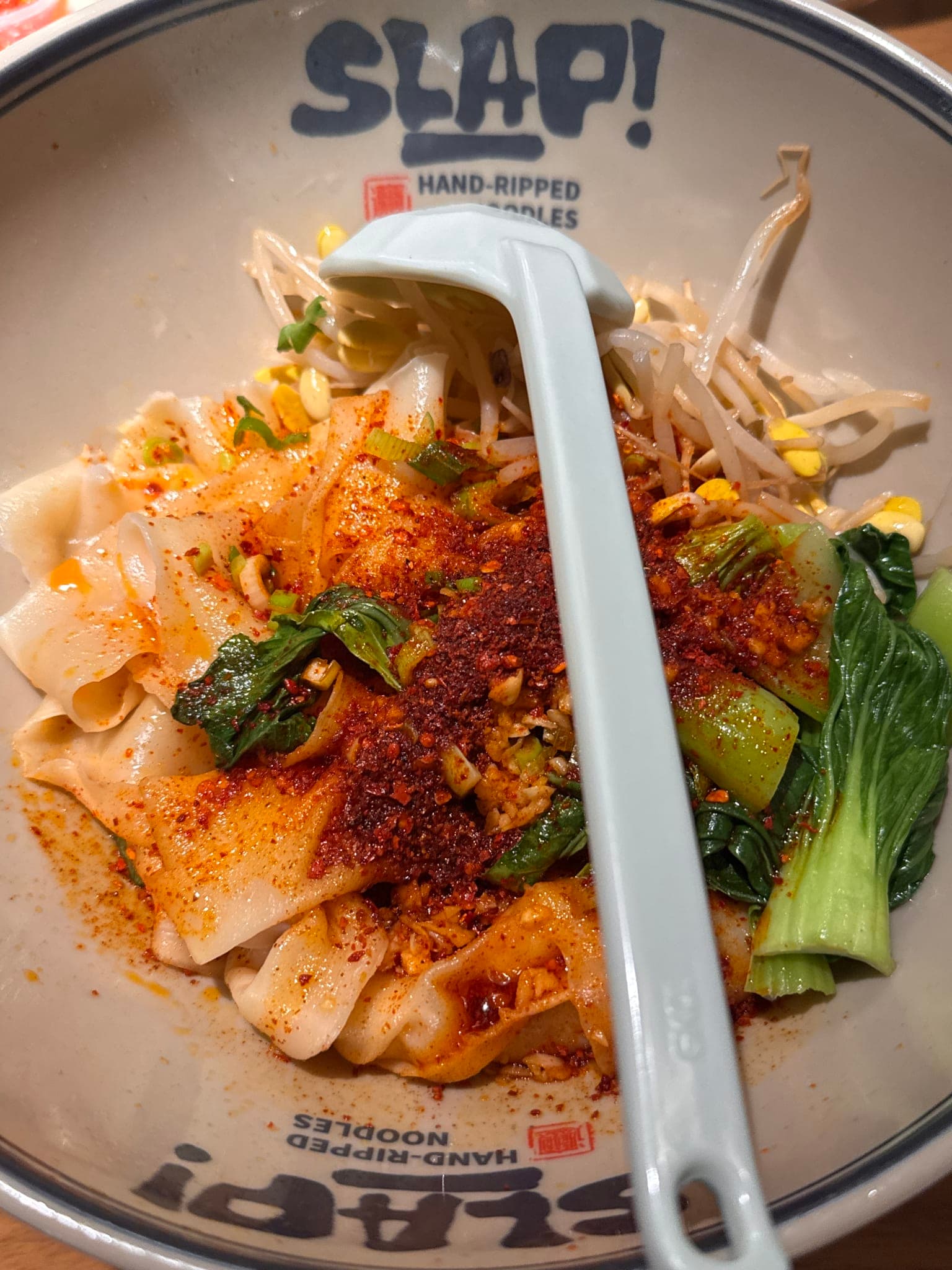 Close-up of wide hand-ripped chili slap noodles with chili oil bean sprouts and bok choy in a SLAP bowl