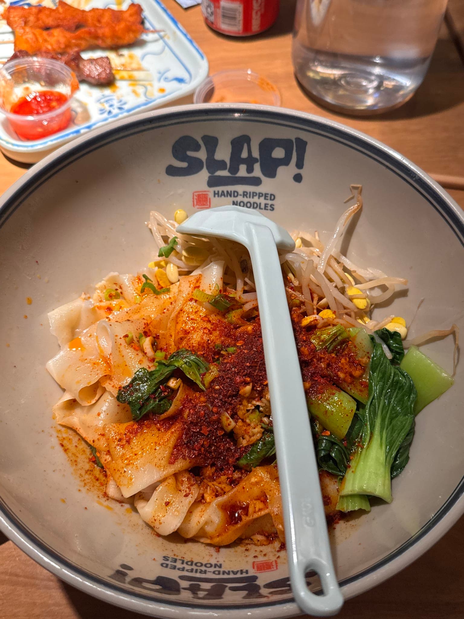 Bowl of wide hand-ripped signature chili slap noodles topped with chili powder bok choy and bean sprouts at SLAP in Orlando