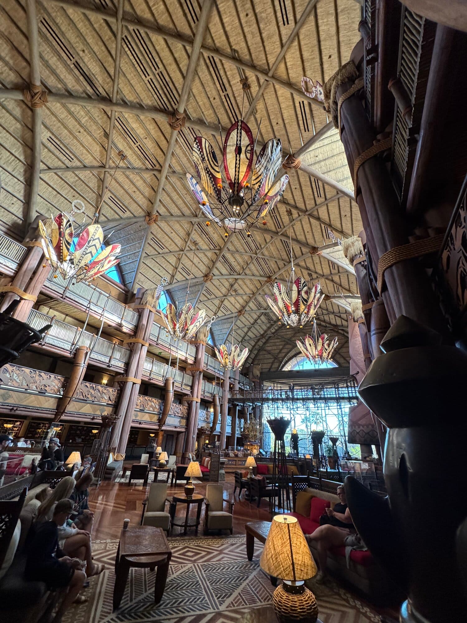 The multi-story lobby atrium of Jambo House at Disney's Animal Kingdom Lodge with colorful African chandeliers and thatched ceiling beams