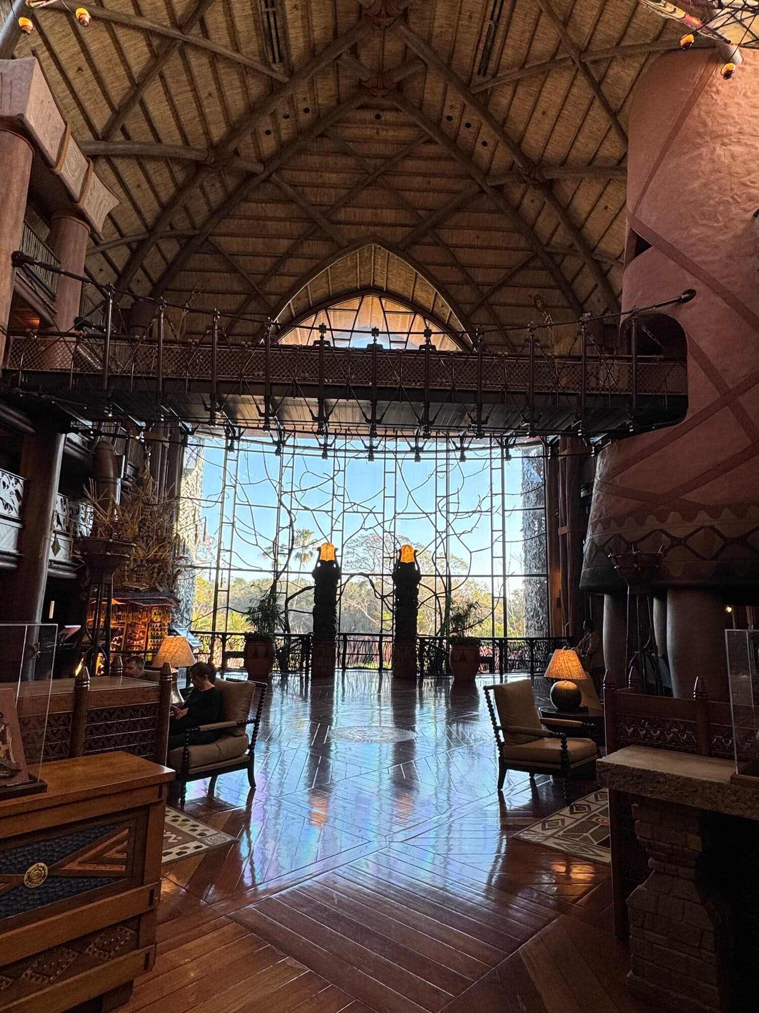 The grand lobby of Jambo House at Disney's Animal Kingdom Lodge looking toward floor-to-ceiling windows overlooking the Uzima Savanna at golden hour