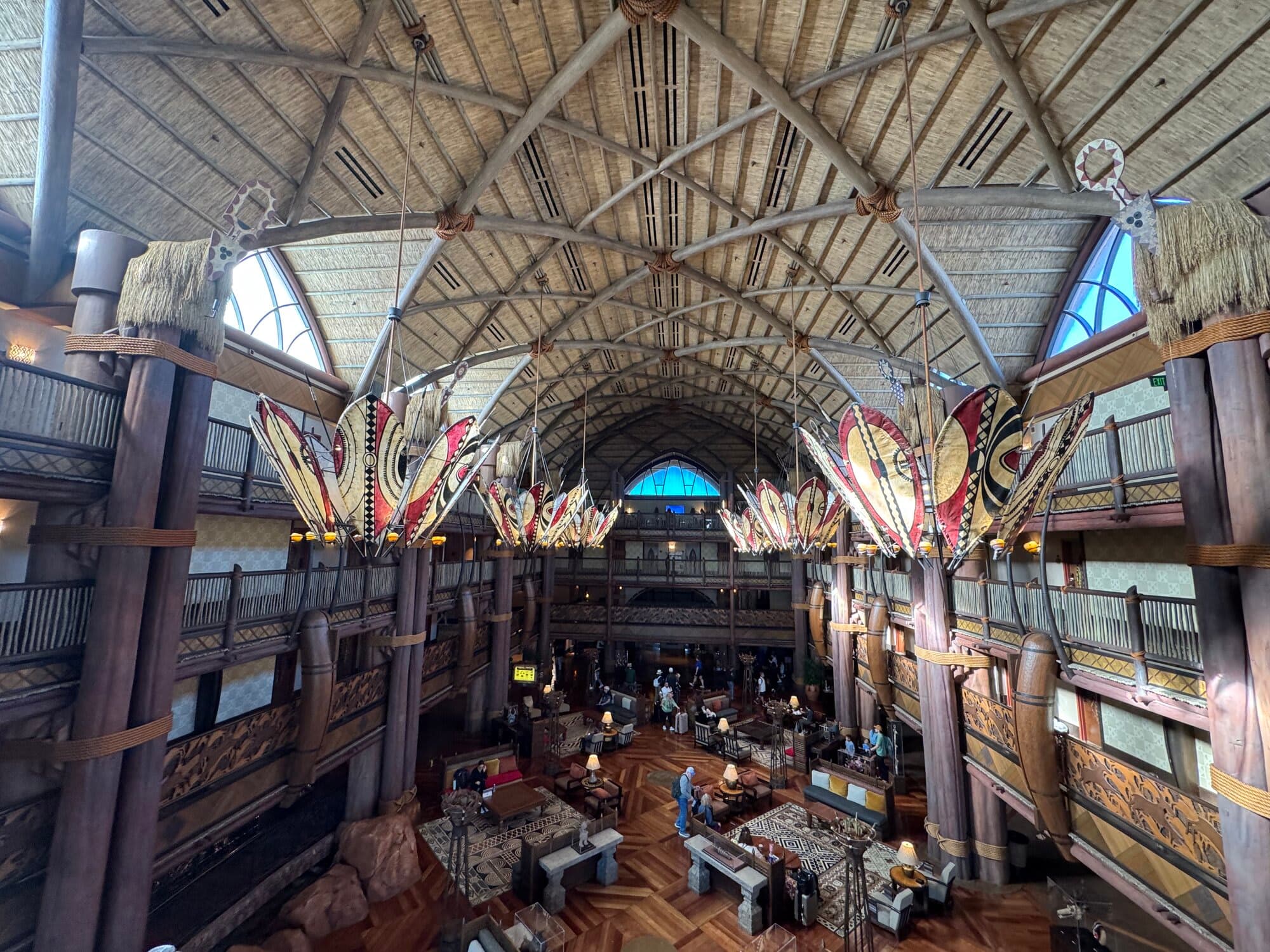 Panoramic view from the upper level of Jambo House lobby showing the full atrium with African chandeliers, carved railings, and the Kilimanjaro Club floor above