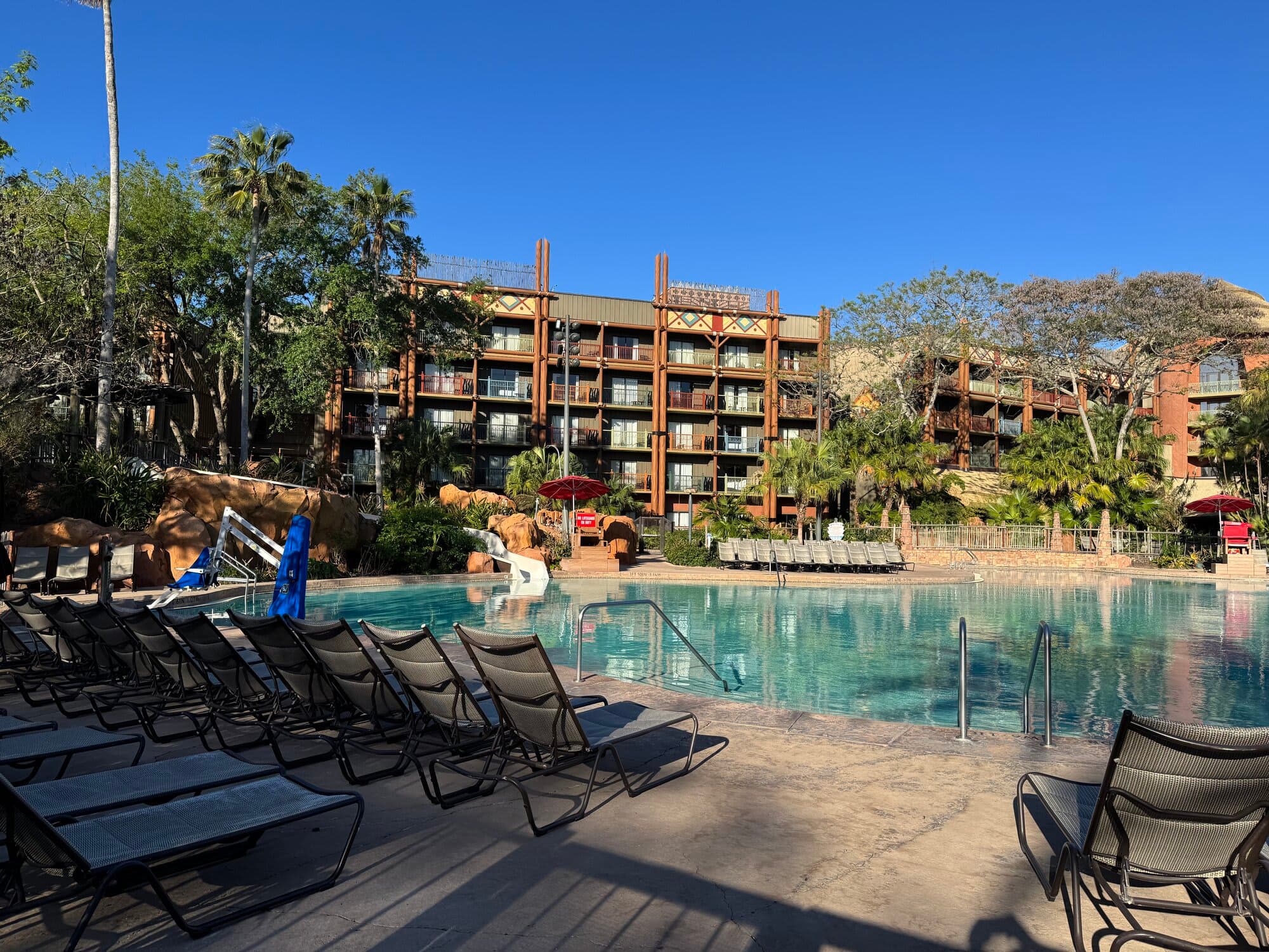 Uzima Springs pool at Jambo House with lounge chairs in the foreground and the Animal Kingdom Lodge building under clear blue sky