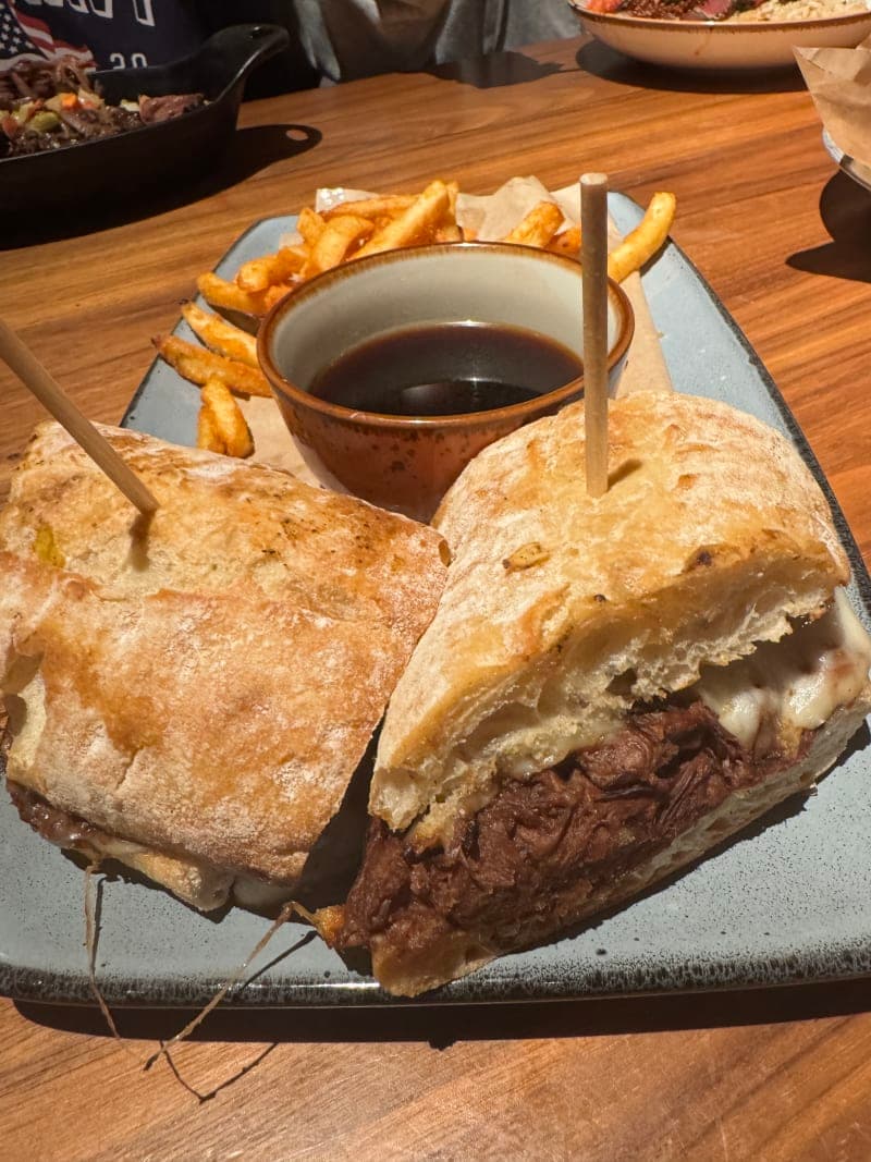 Slow-cooked pot roast dip sandwich with melted mozzarella, caramelized onions, and horseradish cream on a toasted roll, served with au jus for dipping