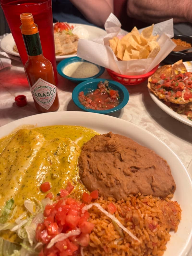 Two Chuy's cheese enchiladas smothered in Boom Boom sauce — a creamy, cheesy roasted green chile and tomatillo sauce — plated on a ceramic dish