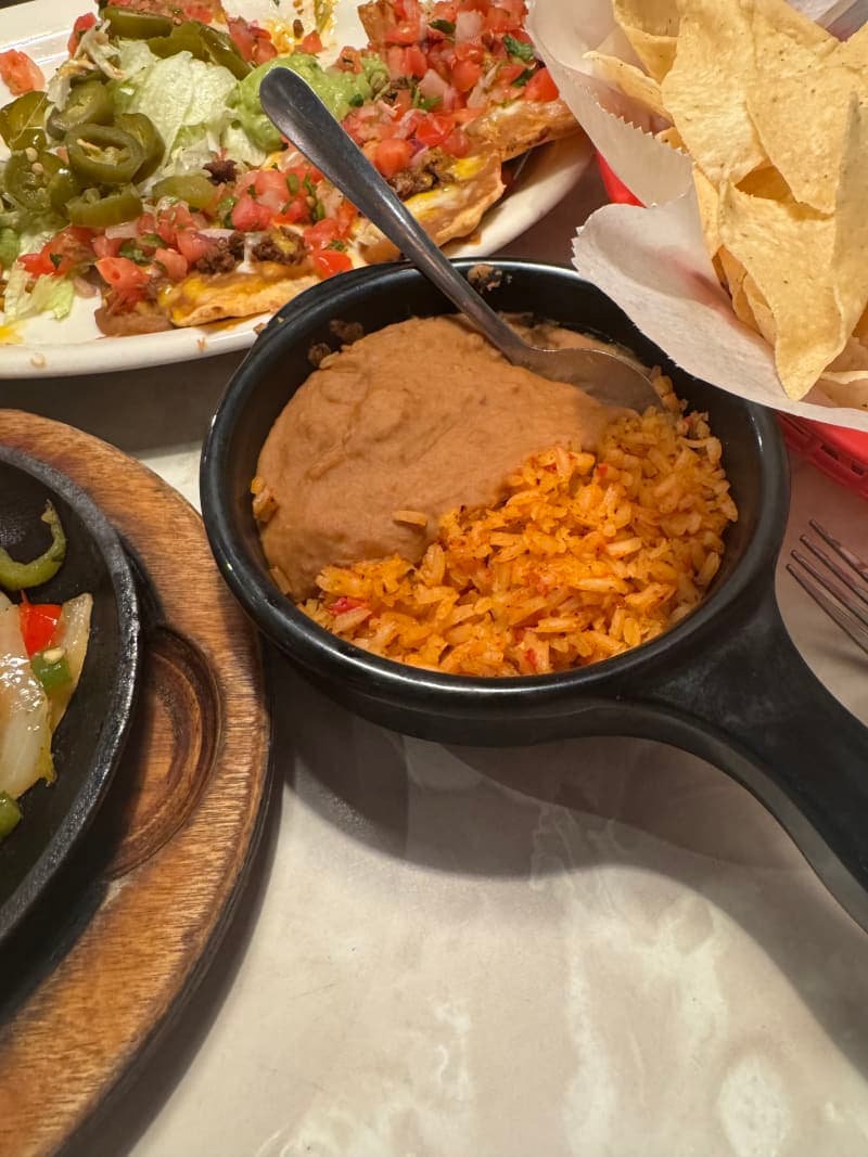 A side serving of Chuy's Mexican rice and creamy refried beans in separate portions on a plate, served alongside the fajita platter