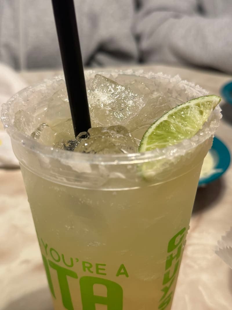 A Chuy's margarita on the rocks in a salt-rimmed glass garnished with a fresh lime wedge